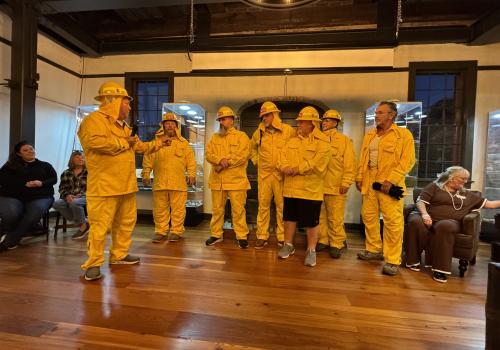 Group in yellow rain gear speaking in a warmly lit room.