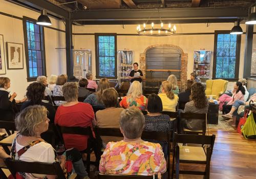 Audience seated in a cozy room, listening to a speaker.